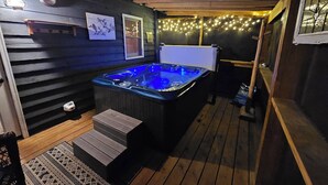 Una terraza de madera con un jacuzzi, escaleras de madera y luces colgantes.