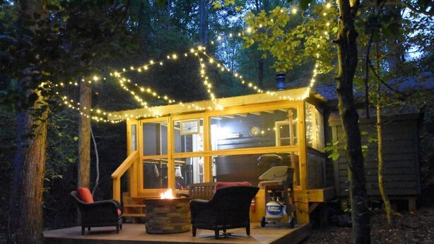 Una cabaña de madera con frente de vidrio, rodeada de árboles y decorada con luces de cadena.