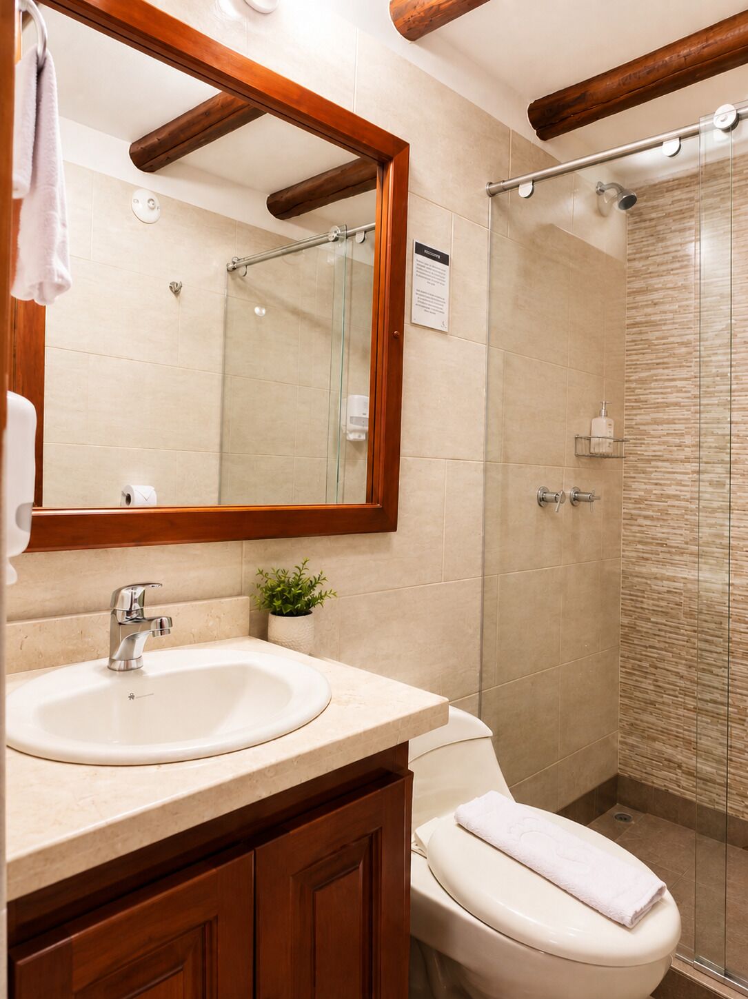 Un baño con tocador de madera, inodoro, ducha con puerta de vidrio y espejo con marco de madera.