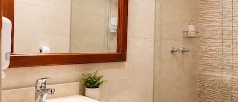 Un baño con tocador de madera, inodoro, ducha con puerta de vidrio y espejo con marco de madera.