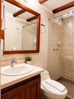 Un baño con tocador de madera, inodoro, ducha con puerta de vidrio y espejo con marco de madera.