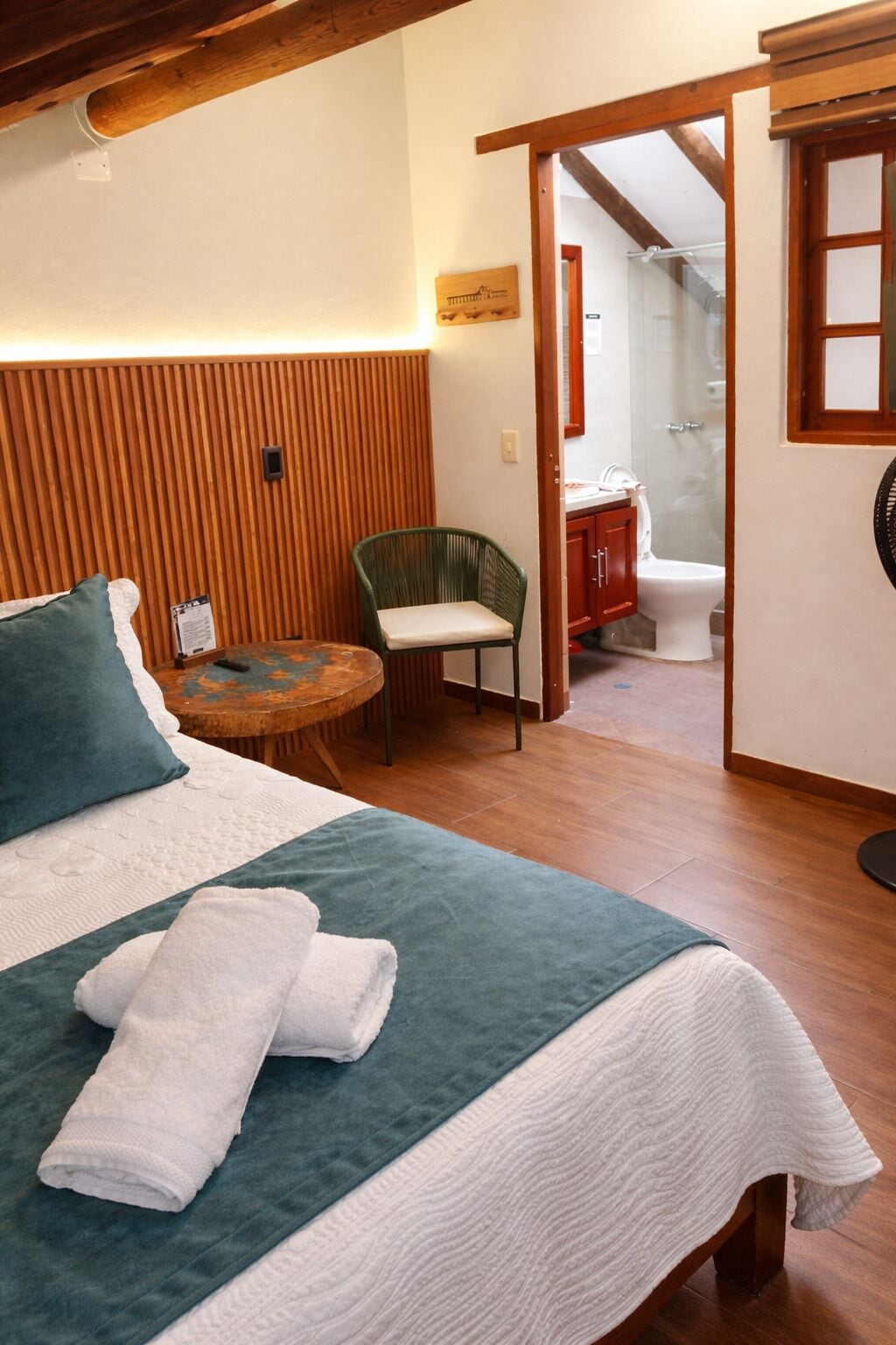 A room with a bed, a chair, a small table, and a bathroom visible through an open door.