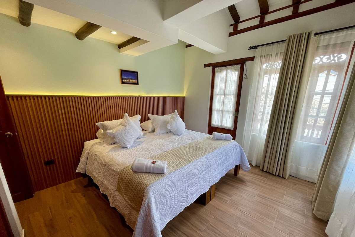 Habitación de hotel con una cama grande, cabecera de madera y vista a la ciudad por la ventana.