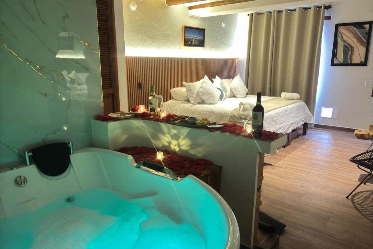Un dormitorio con cama, una botella de vino y una bañera con pétalos de rosa.