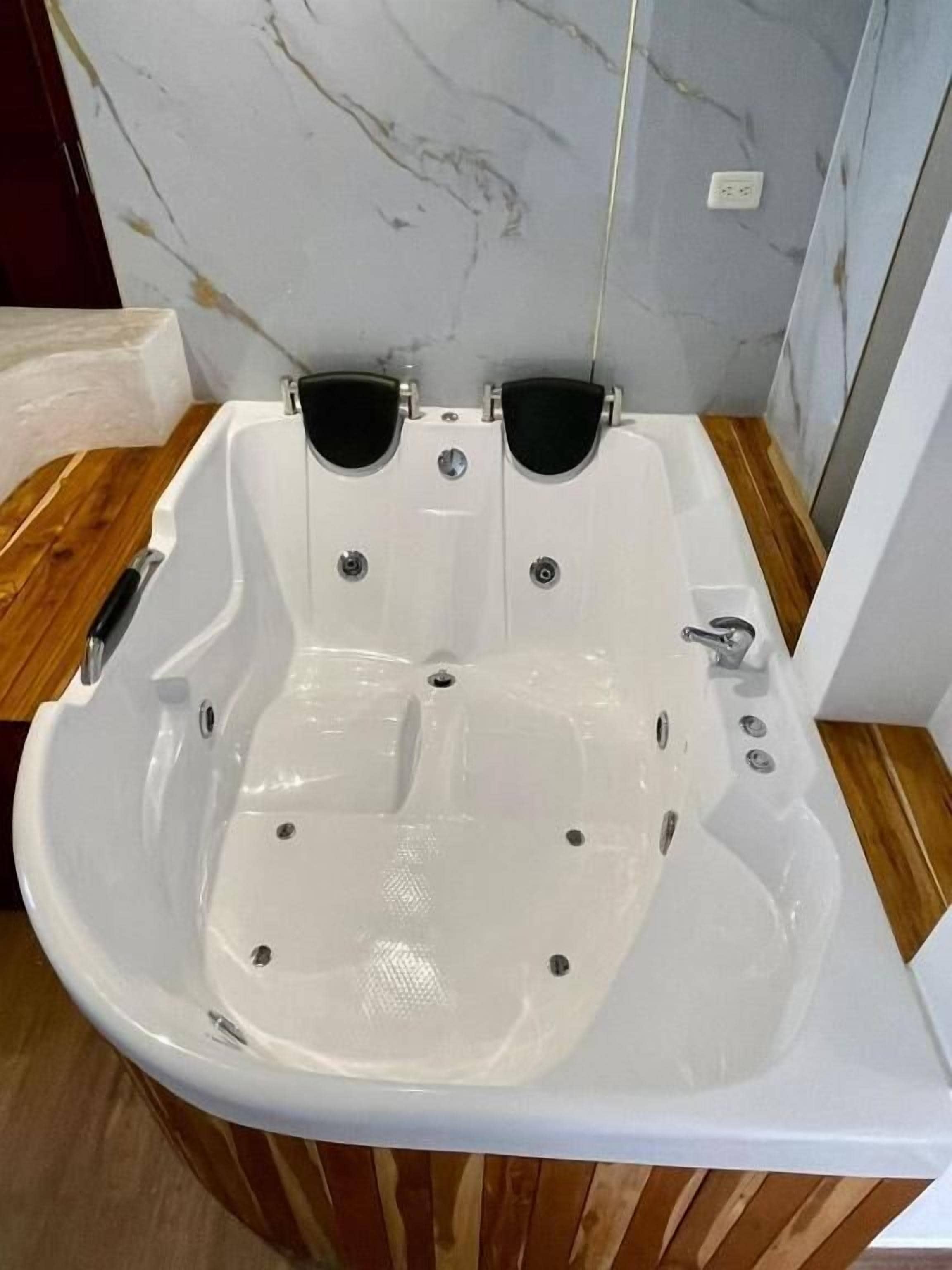 Eine weiße Badewanne mit zwei schwarzen Sitzen, Holzboden und Marmorwand.