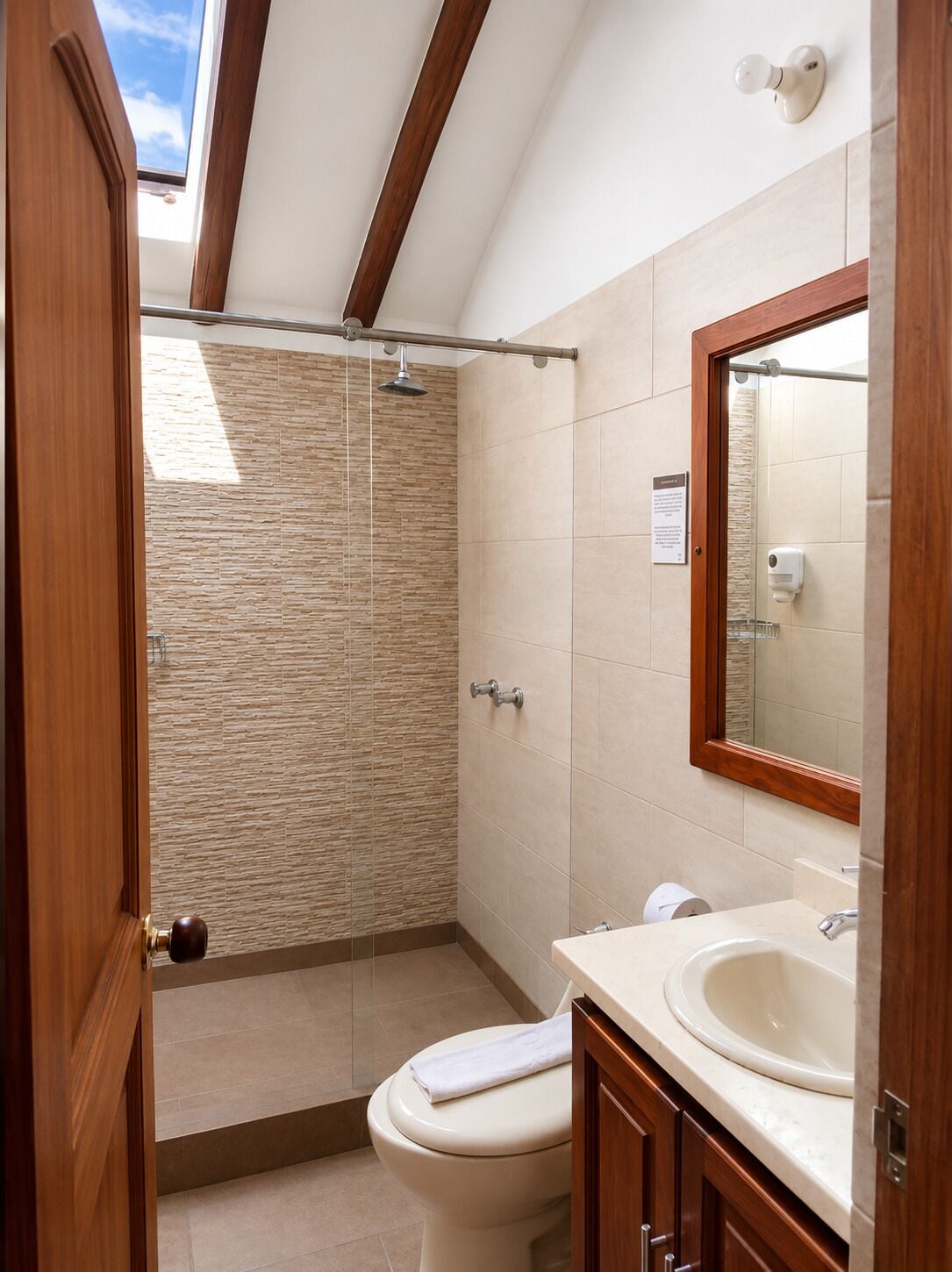 A bathroom with a shower, toilet, and sink, featuring stone wall tiles and wooden beams.