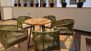 Une terrasse avec une table ronde en bois et des chaises en osier, entourée de plantes en pot.