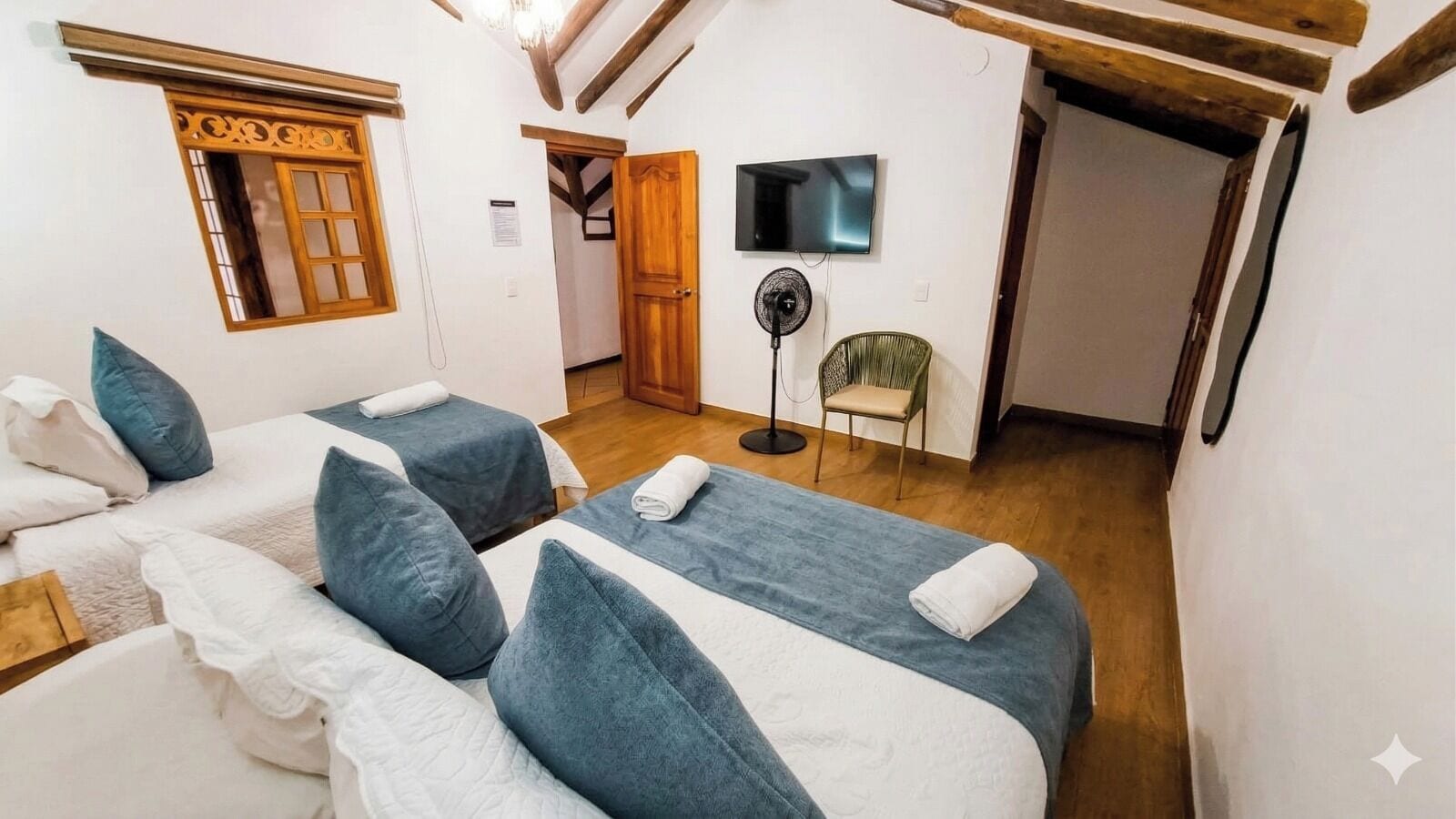 Ein Zimmer mit zwei Betten, einem Fernseher, einem Ventilator und einem Sessel.