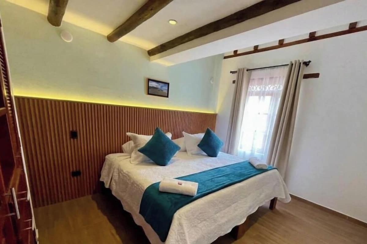 Habitación de hotel con cama, paneles de madera, una ventana con cortinas y un cuadro en la pared.