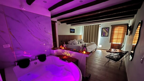 Une salle de bain moderne avec une grande baignoire, un petit coin salon avec une table, et une chambre à coucher avec un lit et une fenêtre.