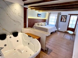 Habitación de hotel con una bañera grande, una cama con cabecero de madera y una mesita con una silla.