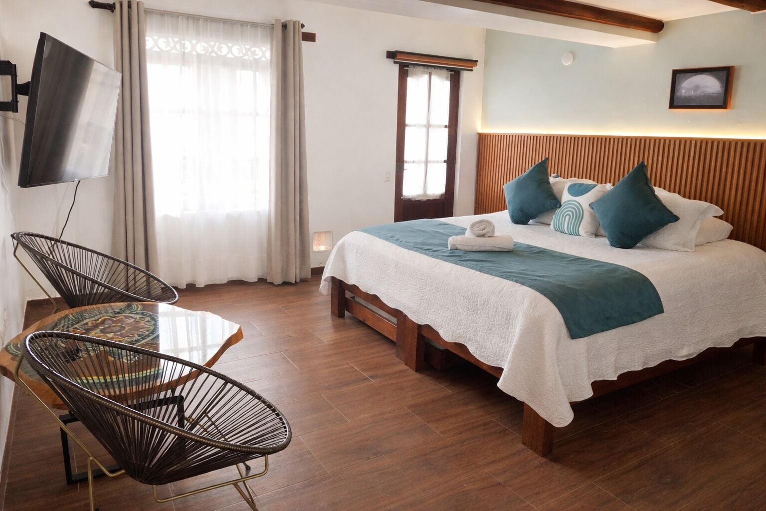 A hotel room with a bed, a TV, a desk with chairs, and a window with curtains.