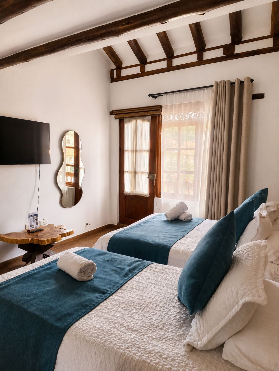 A hotel room with two beds, a TV, a wooden table, and a window with curtains.