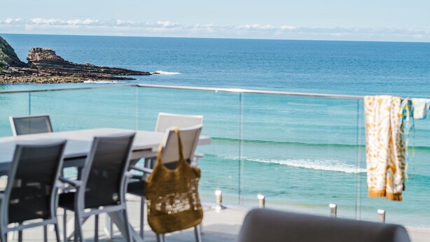 A dining area with a view of the ocean and rocky coastline. - Beach Bliss | Beachfront Luxury w/ Ocean Views (Mollymook Beach)