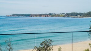 A coastal view with a sandy beach, clear blue sea, and a distant shoreline with buildings. - Beach Bliss | Beachfront Luxury w/ Ocean Views (Mollymook Beach)