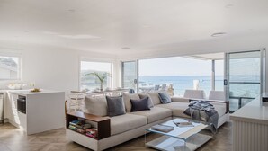 A spacious living area with a large sofa, a glass coffee table, and a view of the sea. - Beach Bliss | Beachfront Luxury w/ Ocean Views (Mollymook Beach)
