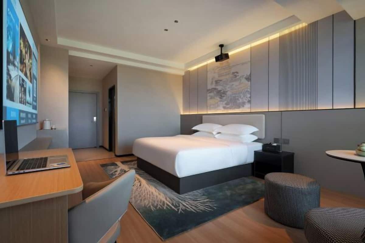 Quarto de hotel moderno com uma cama, uma escrivaninha, um laptop e uma mesinha.