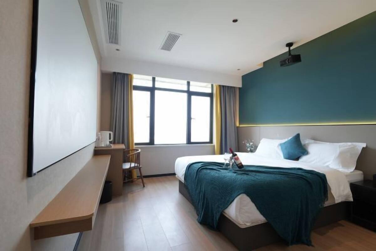 Quarto de hotel com cama, escrivaninha, cadeira, janela e ventoinha no teto.