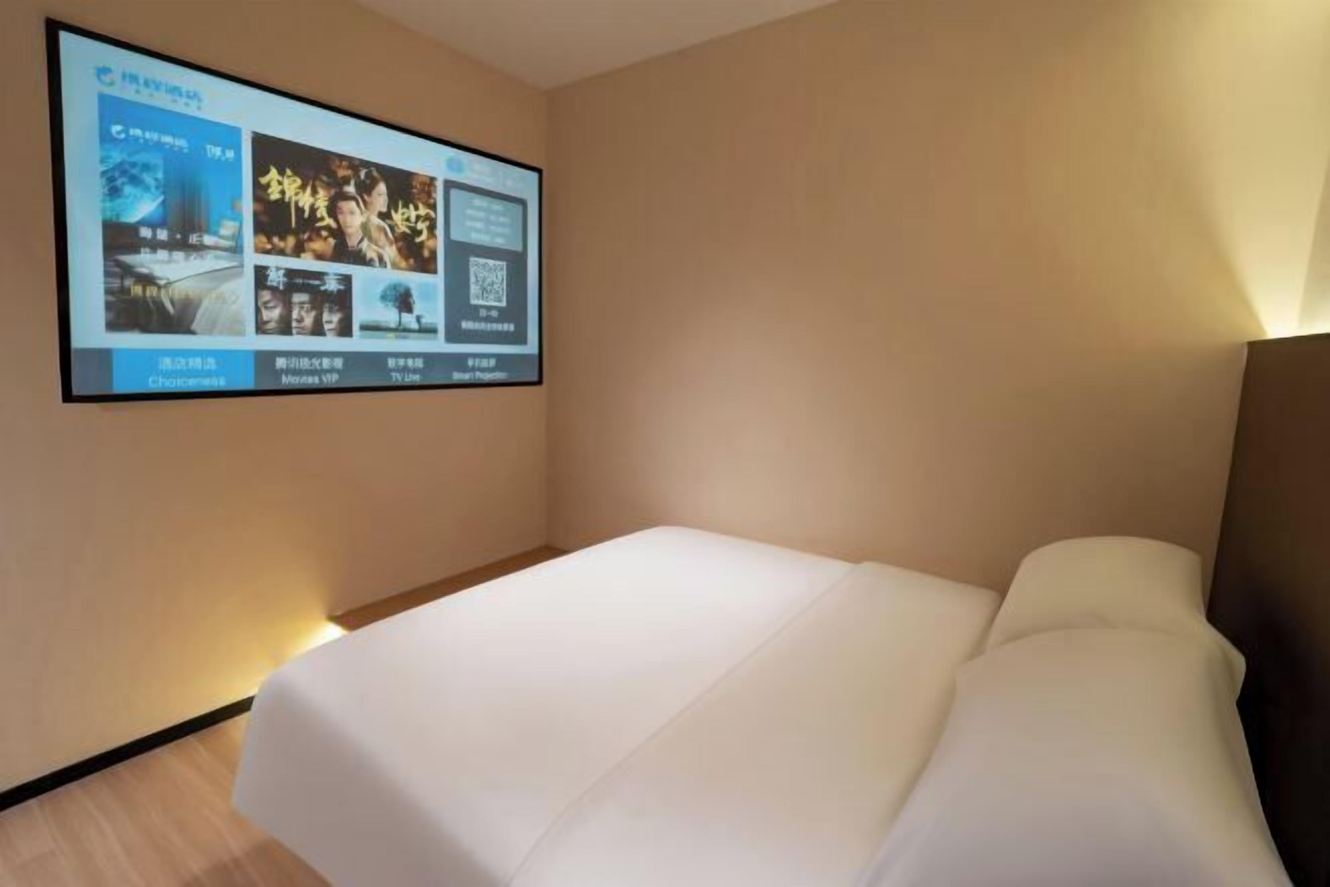 Una habitación de hotel con una cama, un televisor instalado en la pared mostrando opciones de películas y un código QR.