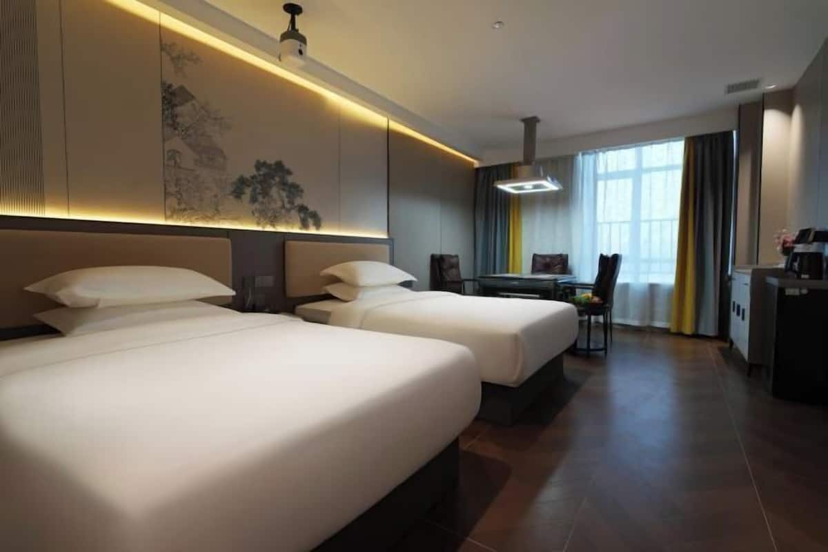 Quarto de hotel com duas camas, uma escrivaninha e uma cadeira.