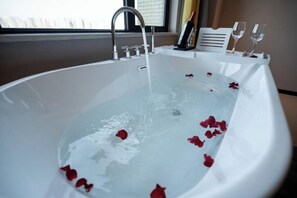 Eine Badewanne, gefüllt mit Wasser und Rosenblättern, mit einem Wasserhahn und einem Tablett mit Gläsern und einer Flasche.