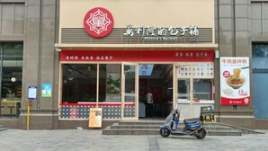 Un restaurante con un letrero rojo y blanco, una moto estacionada adelante y una pizarra con el menú.