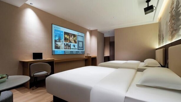 Habitación de hotel con una cama grande, un escritorio y una silla. Hay una pantalla montada en la pared que muestra información.