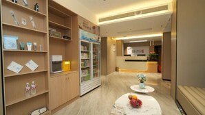 Un hall de hotel con estanterías de madera que exhiben artículos de aseo, un refrigerador con bebidas y un mostrador de recepción.