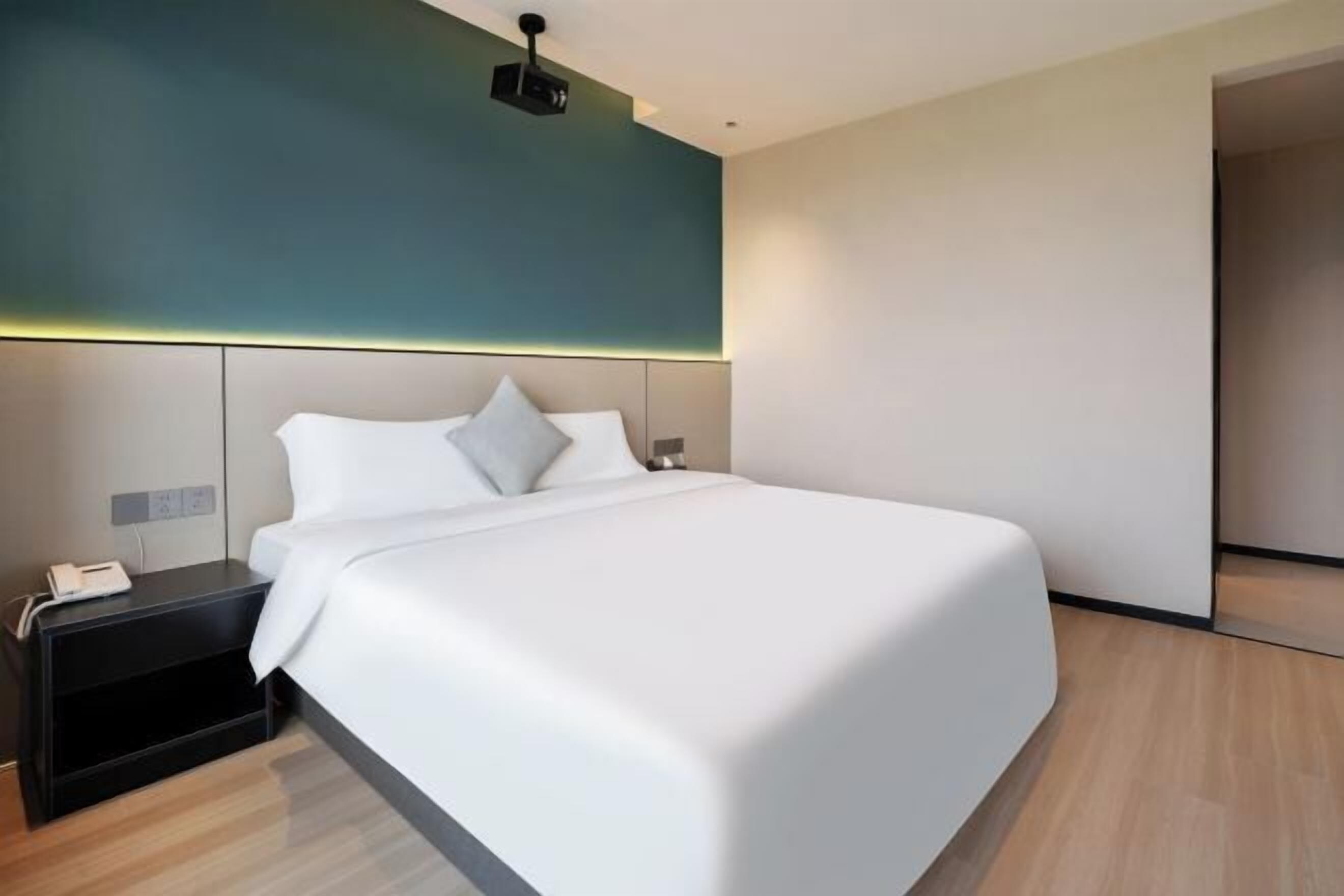 Una habitación de hotel moderna con una cama grande, una mesita de noche con teléfono y un proyector en el techo.