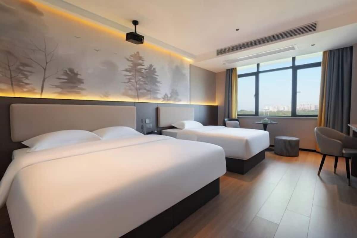 Quarto de hotel com duas camas, uma escrivaninha, uma cadeira e uma janela grande com vista.
