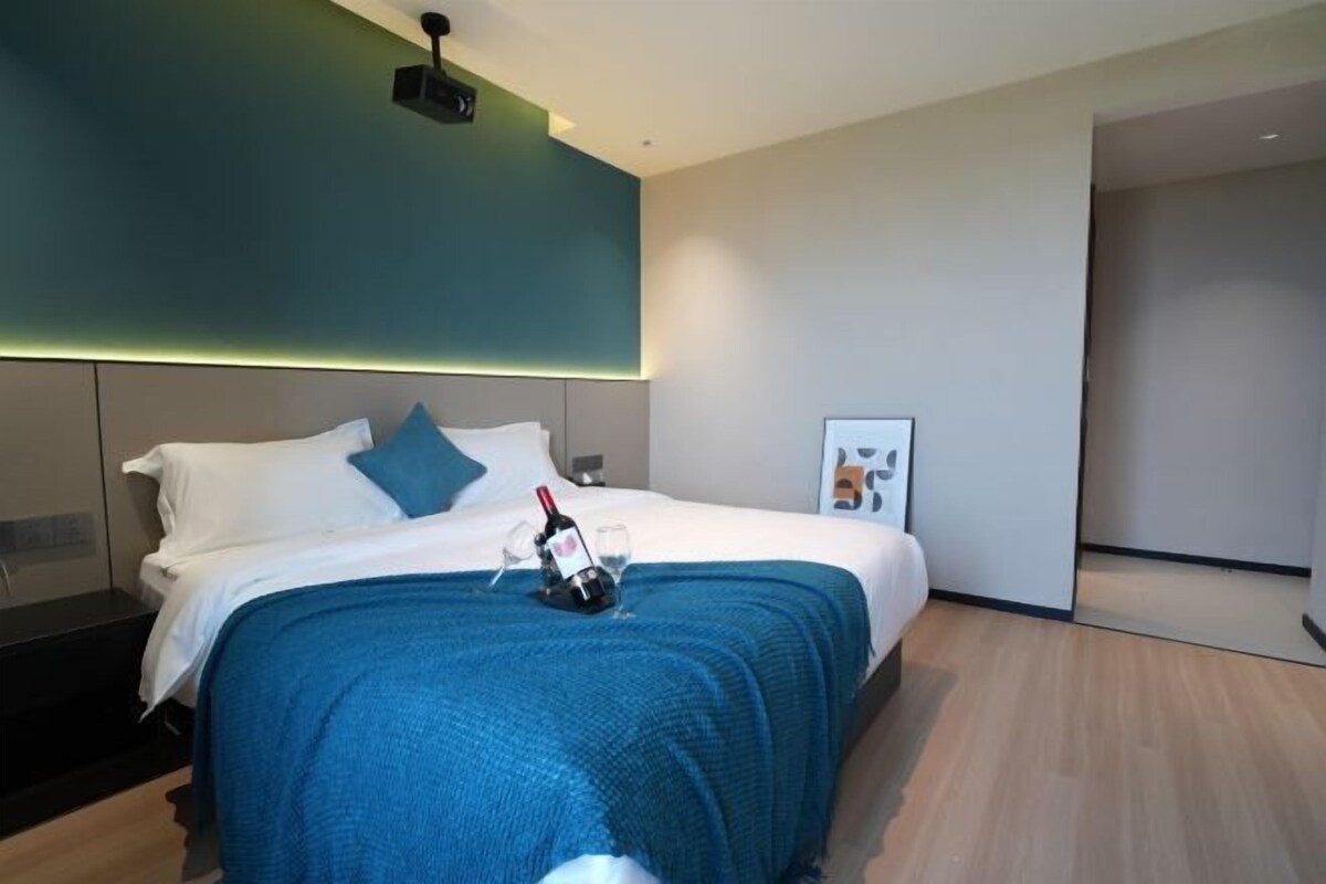 A modern hotel room with a bed, a nightstand, a projector, and a framed picture on the wall.