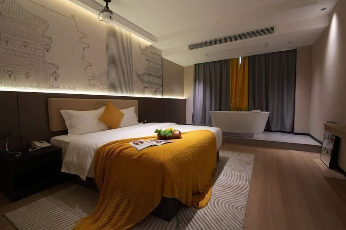 Quarto de hotel moderno com uma cama grande, mesa de cabeceira, casa de banho com banheira e uma janela ampla com cortinas.