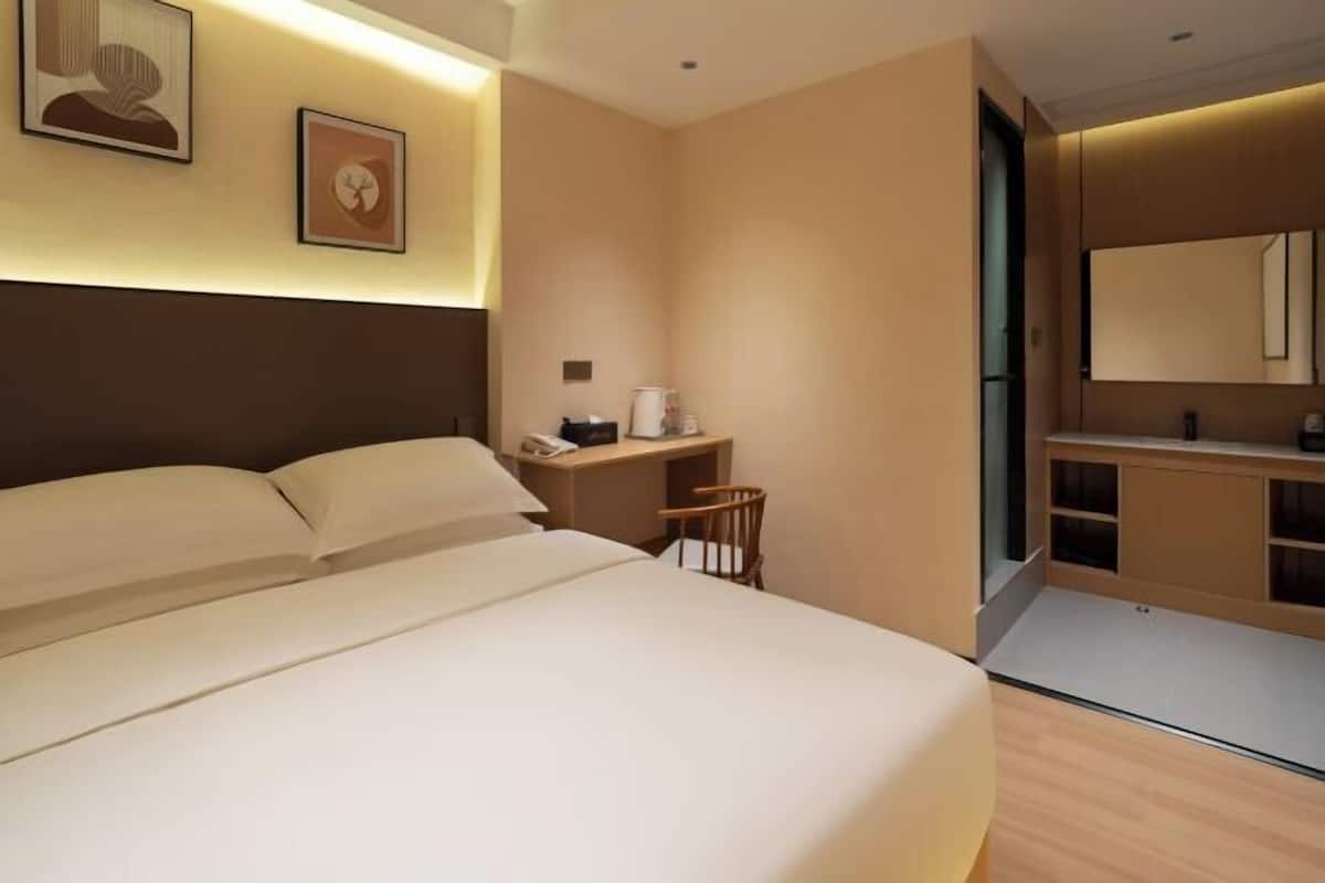 Quarto de hotel moderno com uma cama grande, uma escrivaninha com cadeira, uma mesinha e um espelho.