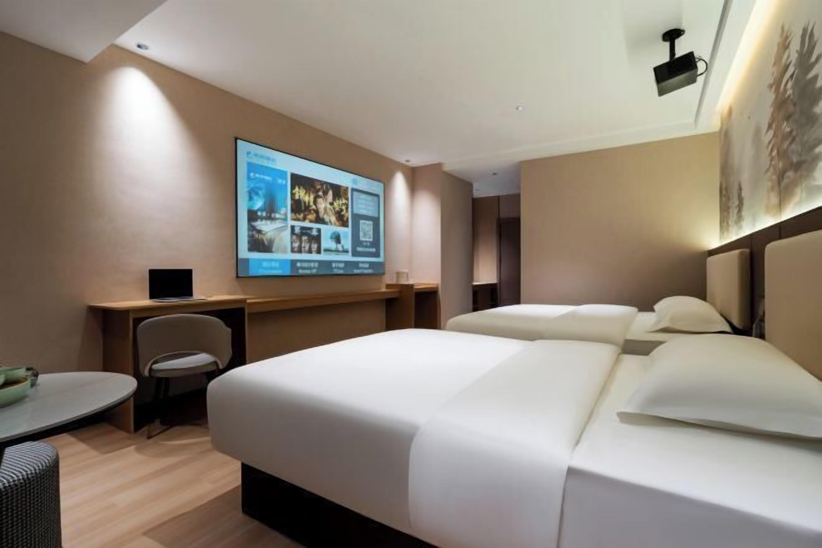 Une chambre d’hôtel avec un grand lit, un bureau, une chaise et un écran fixé au mur qui diffuse du contenu.