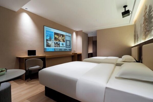 A hotel room with a large bed, a desk, a chair, and a wall-mounted screen displaying content.