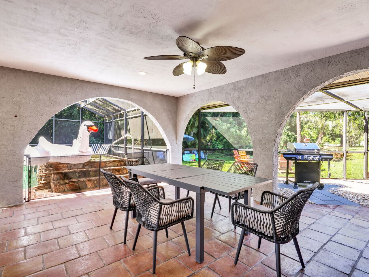An outdoor patio with a table and chairs, a ceiling fan, and a barbecue grill.