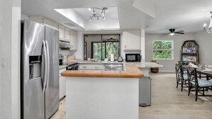 Una cuina moderna amb una illa central, electrodomèstics d'acer inoxidable i una zona de dinar amb un lampadari.