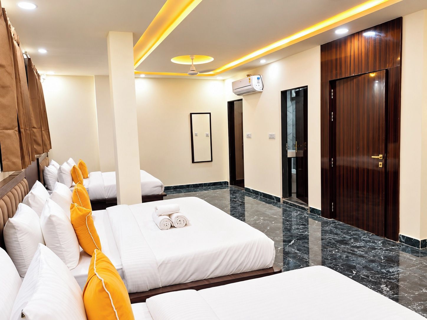 Habitación de hotel con dos camas, ventilador de techo, unidad de aire acondicionado y puerta de madera.