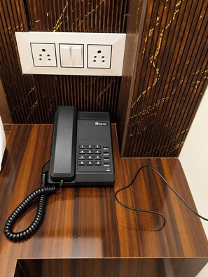 Un téléphone noir à fil, posé sur un bureau en bois, contre un mur orné d’un panneau vertical.