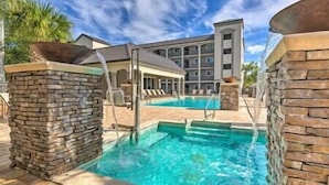 A swimming pool with stone pillars, a covered seating area, and a multi-story building in the background. - D's by the Sea - 3 BR condo steps from the beach (Miramar Beach)