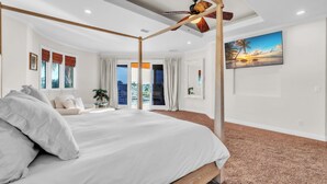 A spacious bedroom with a large bed, a ceiling fan, and a view of the outdoors through large windows.