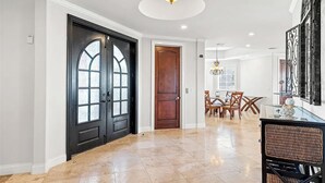 A spacious foyer with a black double door, a wooden door, a dining area with a glass table, and a decorative wall piece.