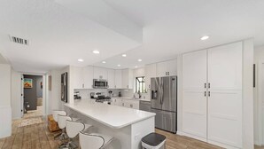A modern kitchen with white cabinetry, stainless steel appliances, and a central island with bar stools. - Cleopatra's Sunset in Ocala (Ocala)