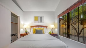A bedroom with a large bed, two bedside lamps, a nightstand, a wardrobe, and a window with a decorative iron grille.