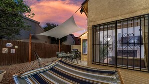 A backyard with a hammock, a table, chairs, and a patio umbrella.