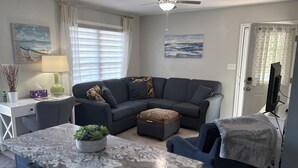 Ein modernes Wohnzimmer mit einer Eckcouch, einem kleinen Tisch, einem Deckenventilator und Kunstwerken an den Wänden.