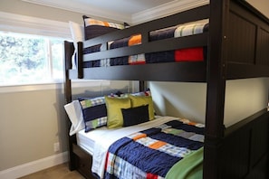A bunk bed with a quilted bedspread and pillows, a window with a view of trees, and a white wall. - Fantastic 6 bedroom 4 bath Pool Home (Anaheim)