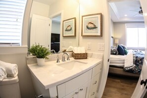 A bathroom with a white sink, a potted plant, and two framed pictures on the wall.