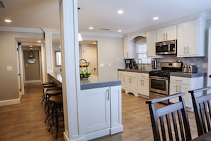 A modern kitchen with white cabinetry, a central island with bar stools, a built-in oven, and a microwave.