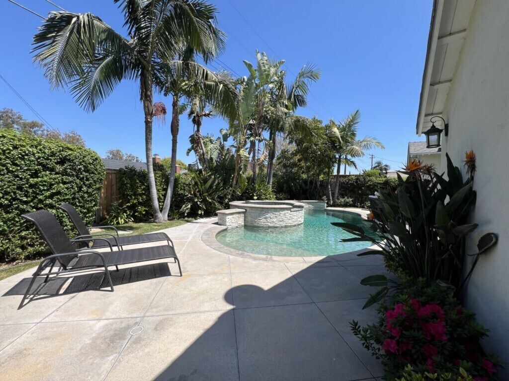 A pool area with lounge chairs, a circular hot tub, and palm trees.